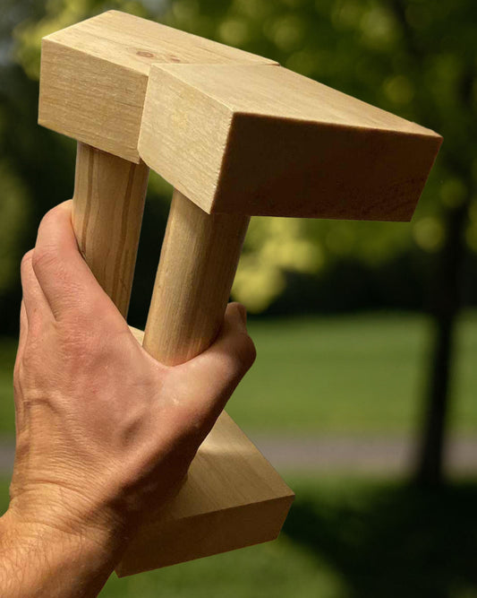 Hand holding a wooden T-shaped tool against a blurred green outdoor background